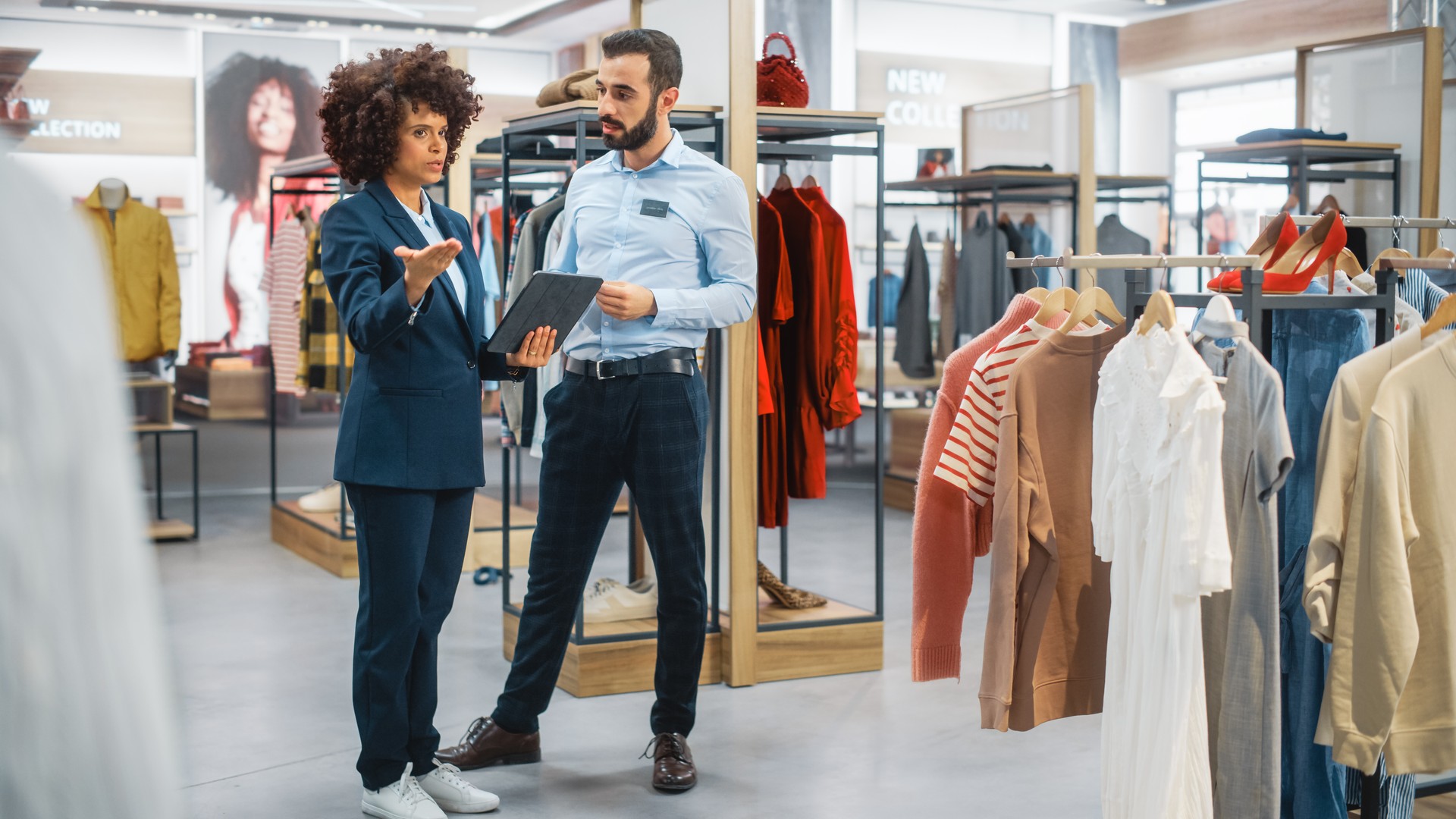 Clothing Store: Businesswoman Uses Tablet Computer, Talks to Visual Merchandising Specialist, Collaborate To Create Stylish Collection. Small Business Fashion Shop Sales Manager Talks to Designer.